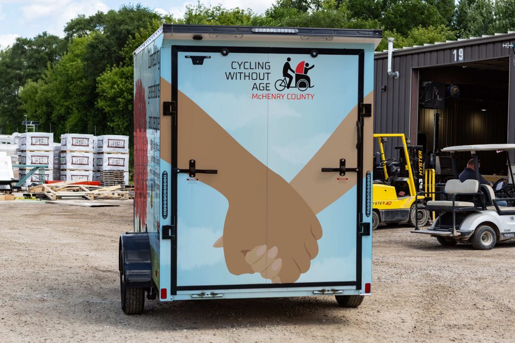 photo of the back of a trailer with a wrap illustration depicting 2 hands holding, advertising cycling without age