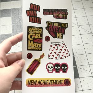 hand holding a 4x7 sticker sheet of different illustrations inspired by the book dungeon crawler carl