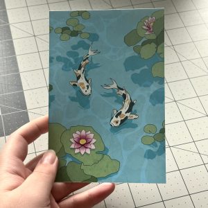 hand holding a 4x6 print of an illustration of koi fish in a pond